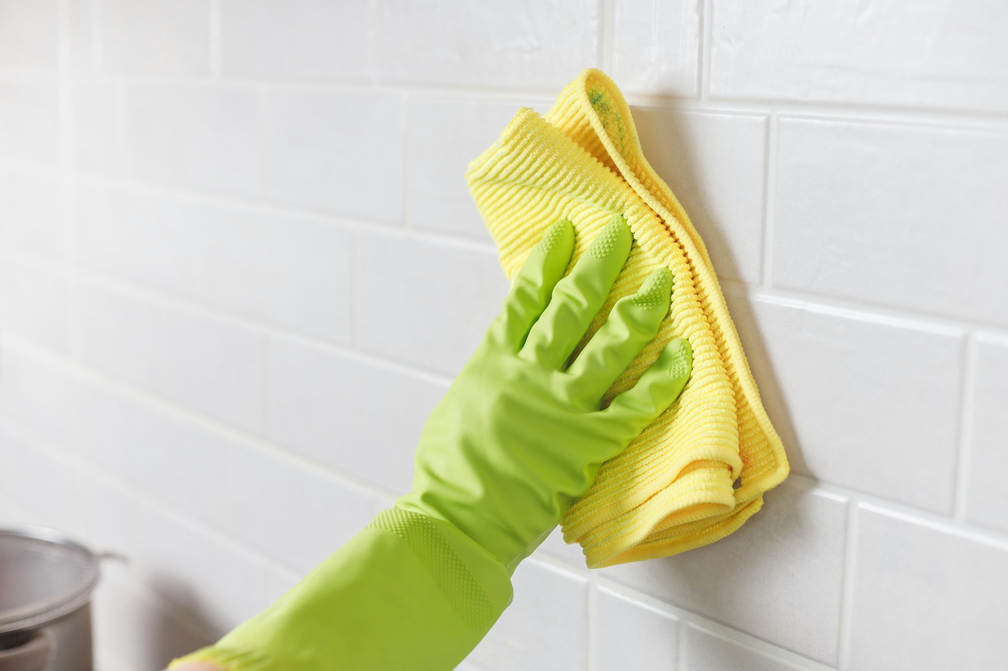 Hand in Gloves Washing White Tiled Wall in Kitchen with Yellow Microfiber